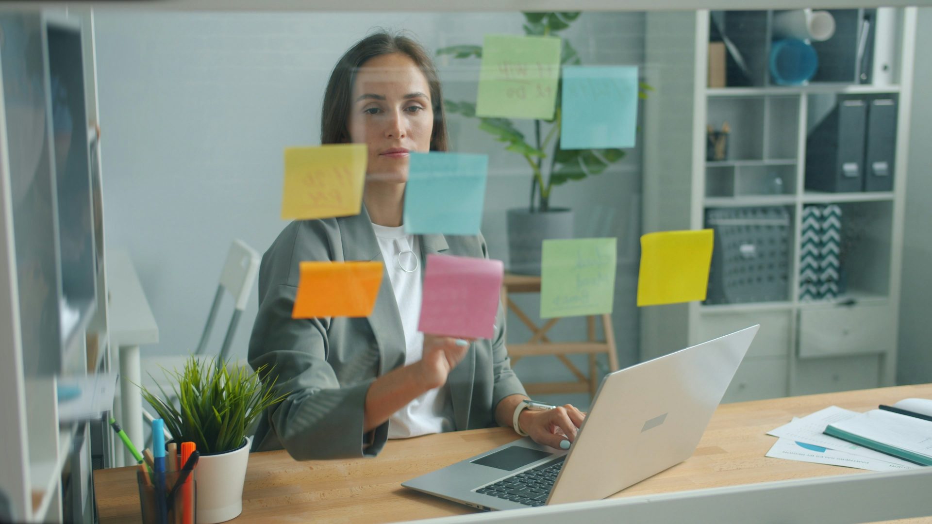 Une femme colle des notes autocollantes sur un tableau en verre.